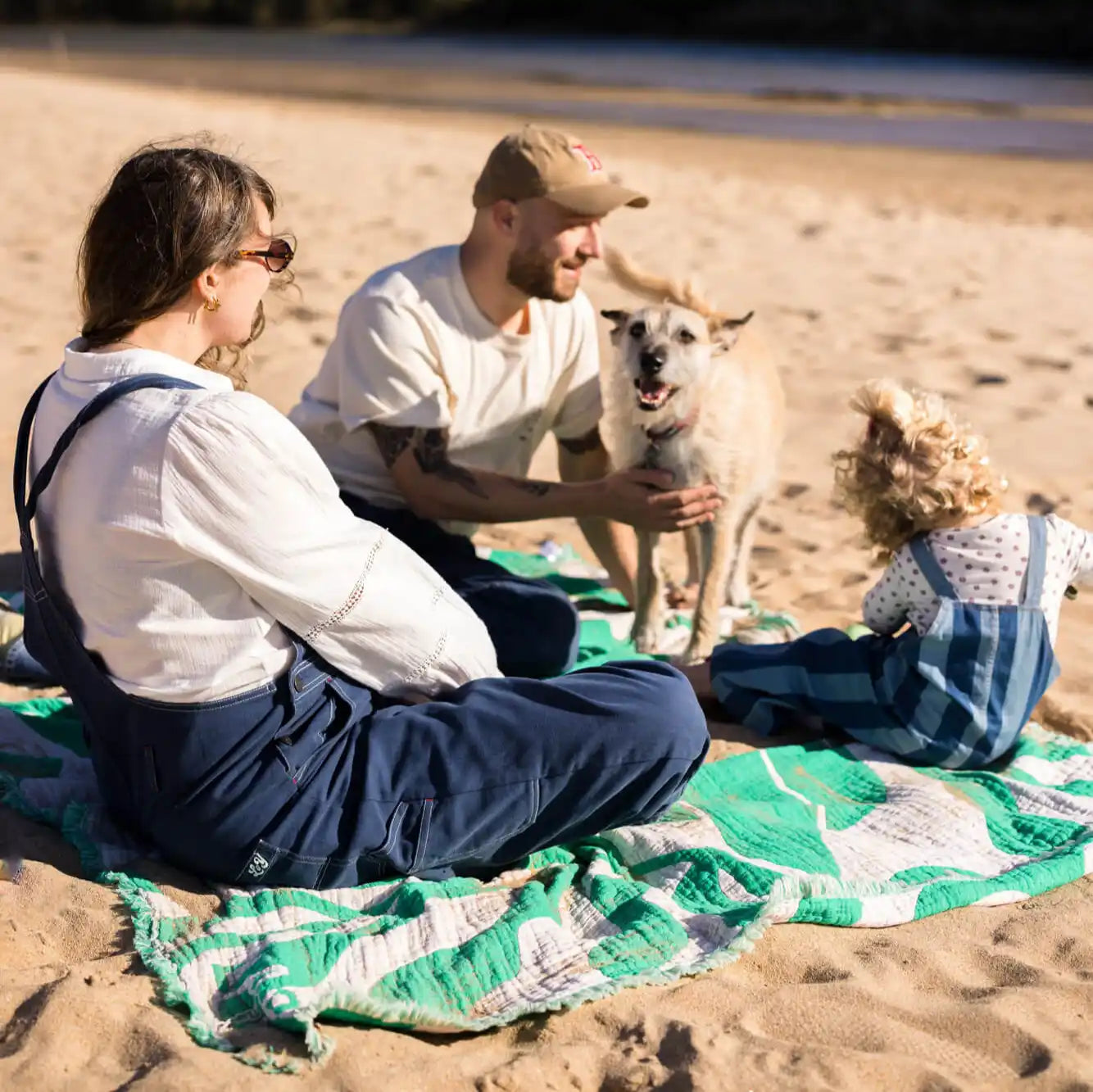 Familie mit Hund am Strand auf grüner Kuscheldecke