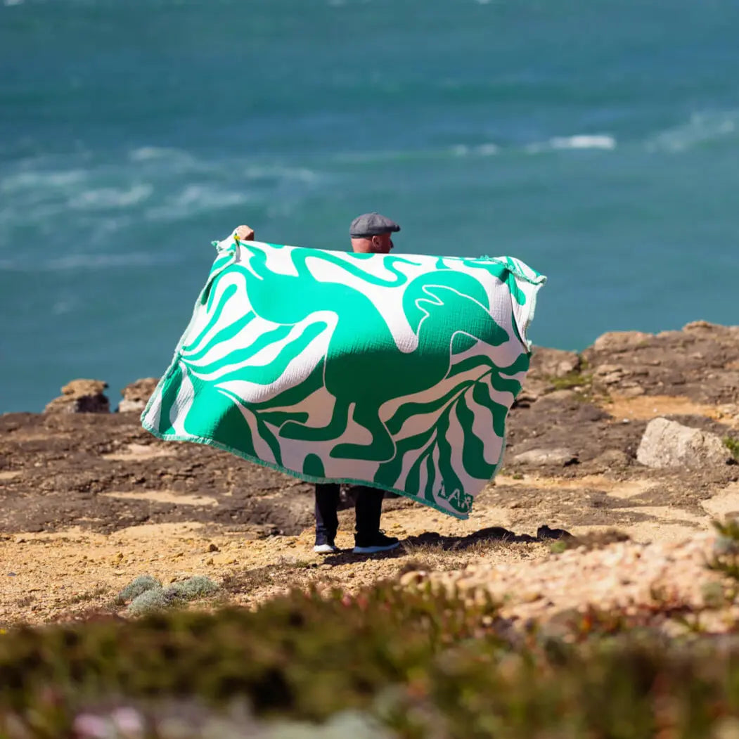 Person hält grüne Kuscheldecke auf den Klippen mit Meerblick in Portugal